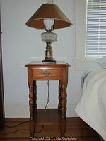 Wooden night stand with single drawer, showing its turned legs and lower shelf, finish shows wear