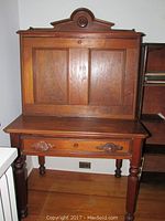 Front view of antique wooden desk with upper back cabinet featuring two paneled doors and decorative top finial.
