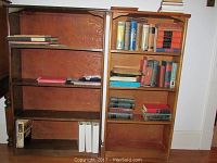 Two wooden bookshelves side by side with books scattered on shelves, showing size and wood finish differences