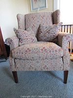 Wingback style chair showing front view with floral fabric and two matching pillows.