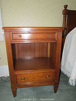 Front view of one wood night stand showing small top drawer, open middle shelf, larger bottom drawer, brass round drawer pulls, and fluted corner detailing.