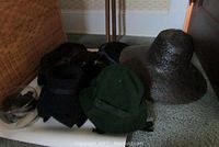 Photo of six vintage ladies hats including a large black textured hat, black and green felt hats, and a red beret on carpet.