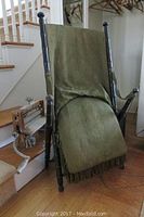Antique folding chair leaning against staircase showing olive green fabric seat and backrest and spindle wooden frame.