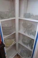 Multiple shelves filled with various clear glass bowls, pitchers, and serving dishes including patterned and footed styles.