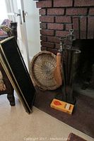 Wide shot showing andirons, woven basket, broom, fire tools, and fireplace screen positioned near the fireplace.