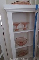 Shelf with various pink Depression glass items including serving bowls and plates.