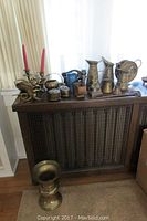 Wide view of assortment arranged on top of wooden lattice cabinet, including pitchers, boxes, candle holders, vase, and dragon bookends.