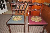 Two wooden chairs with carved backs, different colored needlepoint floral seats (blue and maroon backgrounds).