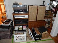Full view of AV rack on top of wood storage cabinet showing turntable, receiver, equalizer, CD player, plus crates of media.