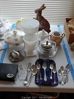 Overview of assorted flatware, decorative covered dish, frosted glass pedestal bowls, ceramic pitcher, clear glass dish with metal lid, wooden rabbit, and Ronson lighter box.