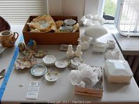 Wide view of assorted milk glass, porcelain Limoges, and salt cellar pieces arranged on table.