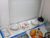 Assortment of cheese dishes and other serving items including glass and ceramic pieces, shown on window ledge and counter.