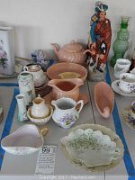 Full view of assorted pink Franciscan pottery including teapot, pitcher, oval bowl, and marked porcelain cups and plates, plus Scottish figurine decanters in colorful Highland attire.