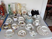 View of assorted bone china teacups, saucers, decorative vases, and black Royal Adderley Scotty dog container on a table