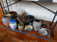 Full view showing multiple ceramic jugs, crocks, vases, and a decorative black coal bucket under a table.