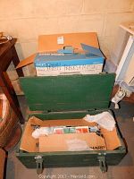 Green wooden carrying case open showing toy train pieces and boxcar inside a cardboard box.