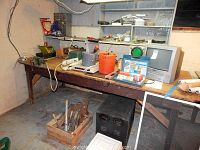 Wide view of wooden workbench holding Toshiba TV/VCR combo, EICO oscilloscope, Memorex Power Center, assorted buckets, cables, and some small tools.