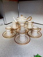 Full coffee set displayed on countertop including coffee pot, six cups and six saucers with gold trim.