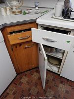 Open wooden and white kitchen cabinets showing stainless flatware, pots, pans, plates, and bowls inside.
