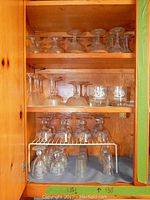 Full wooden cabinet shelf view showing multiple types of glassware including wine glasses, dessert glasses, and tumblers arranged on three shelves.
