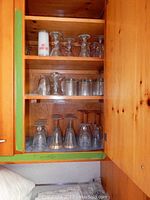 Full view of cabinet with multiple shelves containing sets of various glassware including etched wine glasses, plain stemmed glasses, cordials, and on the rocks glasses.