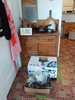 Photo showing wooden cabinet with carved floral accents and vintage kitchen items on top including washboard, grater, food mill, cast iron pan, wooden spoons and utensils.