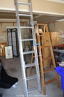 Pair of ladders side by side in storage area showing aluminum extension ladder taller and wooden step ladder shorter