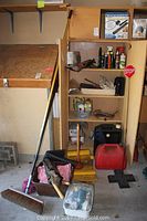 Full view of cabinet and floor area containing tools, cleaning supplies, gas cans, brooms, and other accessories.