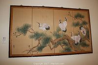 Large four-panel decorative wall screen with cranes on a pine tree branch scene hung on a wall.