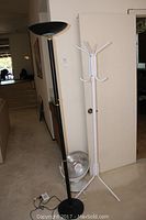 Black halogen torchiere lamp, white coat and hat rack, and small heat dish fan shown together against a white door in a room.