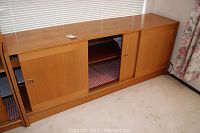 Full view of the maple colored sliding door credenza showing all three sliding doors with one partially open, revealing two shelves inside. It has a Scandinavian design aesthetic and dimensions about 69" wide, 16.5" deep, and 27" high.