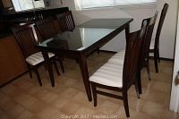 Full view of dark wood dining table with six chairs and glass top