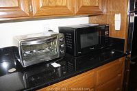 Oster stainless steel toaster oven and black Panasonic microwave oven side by side on kitchen counter with wooden cabinets above.