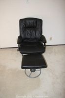 Front view of black patent leather recliner chair with matching ottoman on carpeted floor