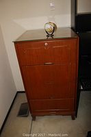 Front view of wood filing cabinet with glass top and mini globe on top.