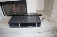 Black laminate stereo console placed on a tiled surface, showing top and front with sliding glass doors and open compartments.