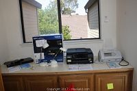 Overall view of fax machine, printer with box, blu-ray player, and two desk lamps on countertop.