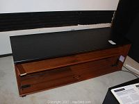 Front and side view showing wooden laminate console table with black painted top and bottom shelves on casters, some wear and scratches visible.