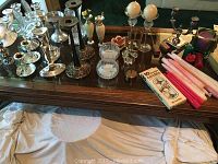 Wide view showing multiple candlesticks of various materials and styles arranged on a wooden table, including silver tone metal, glass, and packaged candles.