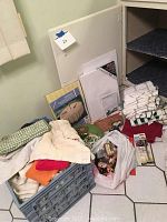 Various fabric pieces, unopened canvas, and miscellaneous items inside a plastic crate and bags, displayed on a tiled floor.