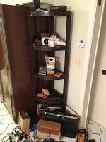Photo of full brown plastic corner shelf with multiple tiers featuring Polaroid camera, vintage camera, eyeglasses, cases, and assorted small items.