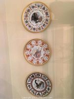 Three collectors plates mounted on wall, detailed traditional biblical and cultural illustrations with gold rims
