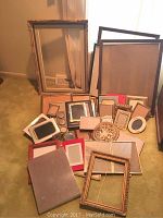 Image showing an assortment of various sized picture frames laid out on the floor including large and small sizes and different shapes like rectangular and oval.