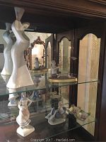 Photo of glass cabinet shelf displaying four white porcelain figurines and one small decorative dish.