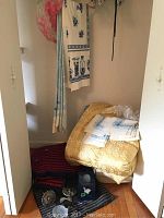 Photo of closet area containing folded yellow/gold damask comforter on floor, hanging striped and floral patterned linens, and small folded cloths.
