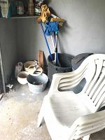 Plastic outdoor chair with black trash cans and gardening tools inside cans in corner of garage