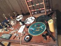 Photo showing wooden chess set board and pieces, several trophies, geodes, decorative plates, candle and various small items on a wooden table.
