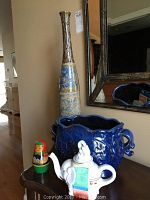 Photo showing the tall ceramic vase, elephant-shaped teapot, ceramic decorative bowl, and Russian nesting dolls on a wooden surface.