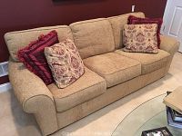 Full view of tan textured Sealy sleeper sofa with 4 throw pillows, showing general shape and fabric texture.