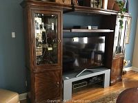 Full view of expandable entertainment center showing central TV space with a flat screen TV, wood curved details, and side display cabinets with beveled glass doors.